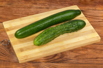 Two whole long cucumbers of different varieties on cutting board