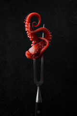 Boiled octopus or squid tentacles on a fork. Isolated on a black background. Close-up. Seafood. © Yaruniv-Studio