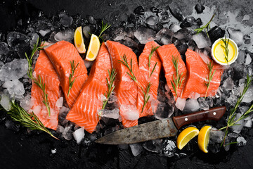 Fresh raw salmon steaks on ice with rosemary and lemon. Fish fillets on black stone background. Top...
