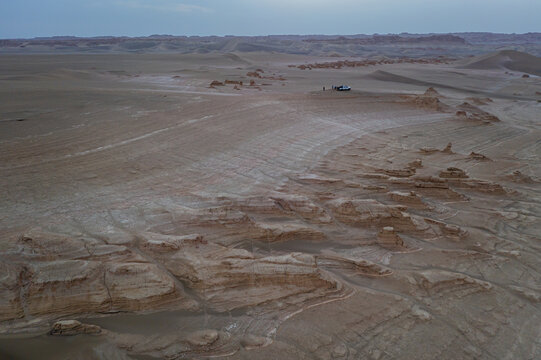 Aerial view of a lone vehicle sits nestled among the wind-carved yardangs, contrasting against the endless expanse of the desert, Kerman, Kerman Province, Iran.
