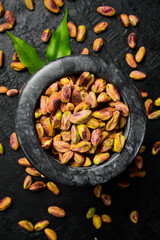 Stone mortar with pistachio kernels, preparation of pistachio flour. Macro photo, close-up, on a black slate table.
