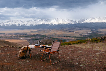 Breakfast outdoors with folding chair and picnic table against snowy mountains, vanlife concept