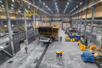 Two engineers control repair of dump car in garage of factory. Industry big yellow mining truck...