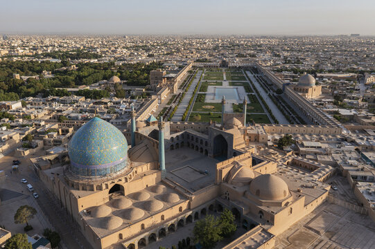 Aerial view of the mesmerizing blue-tiled dome of the Shah Mosque contrasts with the golden hues of Naqsh-e Jahan Square, a tapestry of history and vibrant life, Isfahan, Isfahan Province, Iran.