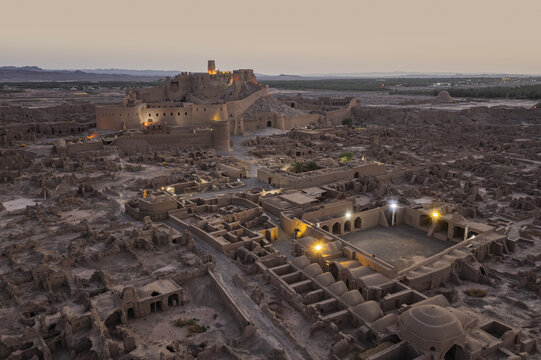 Aerial view of the ancient Arg-e Bam citadel glowing warmly against the cool twilight sky, a testament to history and resilience, Bam, Kerman Province, Iran.