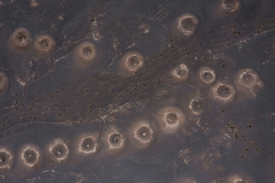 Aerial view of mysterious circular structures puncturing the arid landscape, their pale rims stark against the dark earth, creating an alien vista, Bam, Kerman Province, Iran.