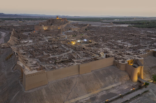 Aerial view of the ancient Arg-e Bam citadel's mud-brick walls and ruins glow softly under the evening sky, a testament to enduring history, Bam County, Kerman Province, Iran.