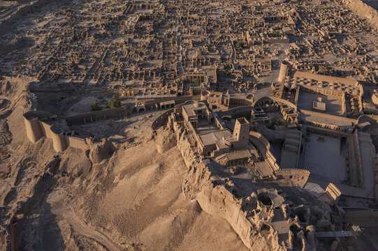 Aerial view of the sun-baked Arg-e Bam citadel, a majestic ruin against the desert landscape, its mud-brick walls whispering tales of ancient Persia, Bam, Kerman Province, Iran.