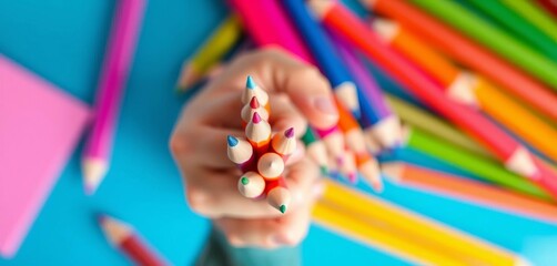 Obraz premium Close-up hand gently holding colorful pencils against a vibrant blue backdrop, childhood, creative