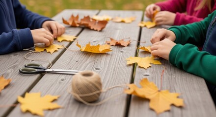 Children crafting autumn leaf garland outdoors on wooden table
