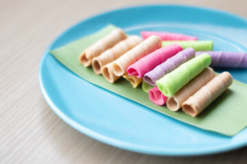 Colorful Thai rolled wafer snacks neatly arranged on banana leaf over a blue plate. Traditional Asian dessert with pastel colors, crispy texture, and sweet taste.
