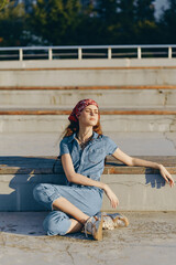 lifestyle woman in modern boho-western denim street style sits relaxed outdoors in warm sunlight...