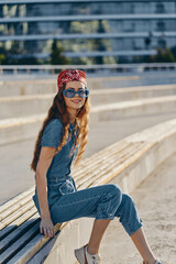 Lifestyle woman in modern boho-western denim street style wearing vintage sunglasses and a red...