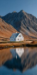 White wooden house with grey roof sits by calm water reflecting mountains and sky