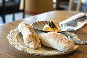 Rustic freshly baked loaves of bread served with creamy gourmet butter on elegant dishware on wooden table