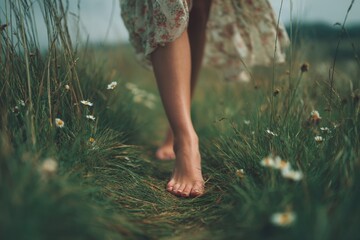 A person strolls barefoot along a grassy path adorned with daisies, enjoying nature's tranquility on a peaceful day