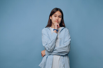 thoughtful young woman shows a contemplative expression on light blue background