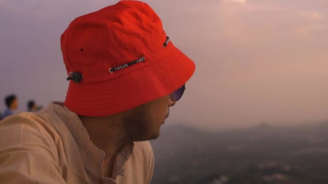 Close-up of a handsome Indian man enjoying the sunset while sitting on the wall of a fort in Udaipur, Rajasthan, India. He is relaxing during his holiday, with a stunning sunset over the fort.