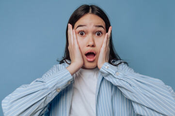 young woman, eyes wide open and mouth opened, expresses sheer astonishment and surprise on light...