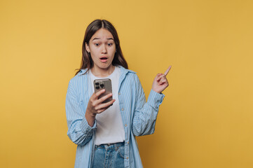 surprised expression graces a young woman's face as she examines her phone, capturing a moment of...