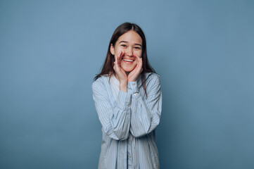joyful young woman embraces excitement by cupping her hands around her mouth, ready to share great news on light blue background