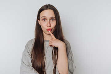 young woman with a contemplative expression touches her finger to her lips, representing...