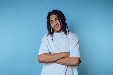 fashionable young man with braided hair poses confidently against a bright blue background,...