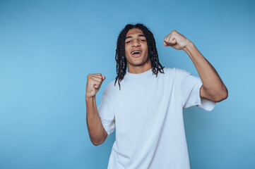 young man expresses joy and victory while smiling and celebrating with his fists raised high on...