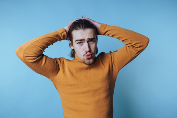 young man poses playfully, making a teasing pout with his hands behind his head, conveying a fun...
