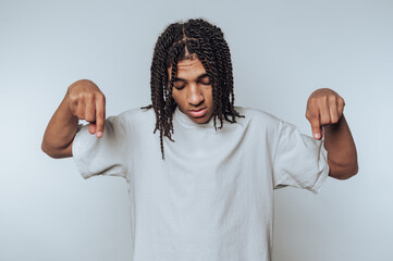 young individual stands with a neutral expression, pointing downward on white background