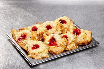 Freshly baked dessert items featuring dough topped with pineapple and colorful jelly are arranged neatly on a tray in a warm bakery kitchen