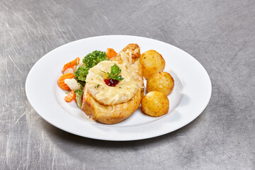 A beautifully arranged plate features roasted chicken topped with a creamy sauce, accompanied by vibrant vegetables and crispy potato balls. The warm lighting adds to the inviting atmosphere