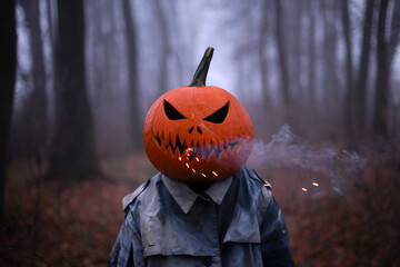 Spooky figure with pumpkin head smoking with smoke and sparks in the misty autumn forest. Scary...