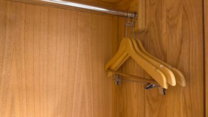 The interior of a modern wooden wardrobe shows a metal hanging rod with two empty wooden hangers....