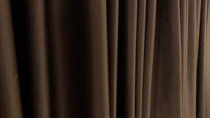 A dark, richly textured curtain hangs vertically, displaying soft folds and subtle highlights, suggesting a stage backdrop, window covering, or elegant room divider