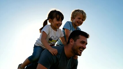 Happy father piggybacking his children against a clear blue sky background