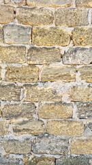 Old stone wall texture with irregular yellow and grey bricks and visible cement joints. Vertical...