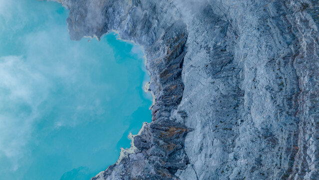 Aerial view of the turquoise lake nestled beside the rugged cliffs of Ijen Volcano Crater, creating a stark contrast of colors and textures, Ijen Volcano Crater, East Java, Indonesia.