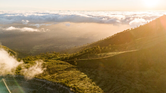Aerial view of verdant hillsides meeting a sea of clouds under a radiant sun, Ijen Volcano Crater, East Java, Indonesia.