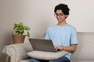 Technology and education concept.. Indian teenage boy studying online at home. Happy young man working on laptop computer