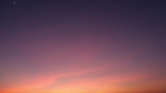 A serene sunrise sky timelapse showing a gentle gradient from warm golden hues at the horizon to soft purples higher up, with delicate clouds glowing softly in the morning light. Time-lapse.
