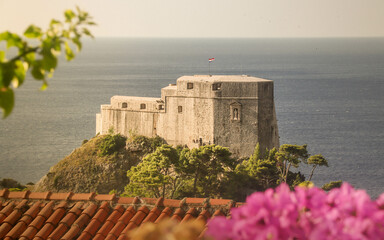 A beautiful castle overlooking the sea, framed naturally by lush greenery and vibrant pink flowers...