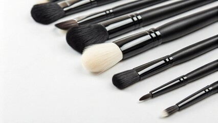 A variety of makeup brushes with black handles and white bristles are arranged on a white...