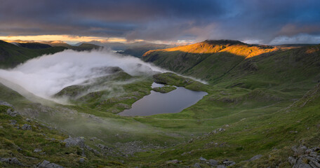 Dramatic view overlooking Sprinkling Tarn with golden light on mountains in The Lake District, UK.