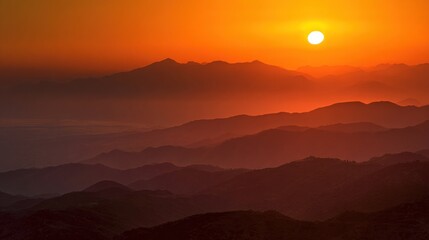 Fototapeta premium Sunset Glow Over Mountain Ranges with Hazy Layers and Fiery Orange Sky