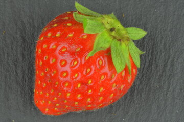 Macro shot of a ripe red strawberry on a black background. Ripe strawberry on a black slate backdrop. Close-up and top view