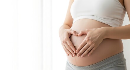 Pregnant woman cradling her belly in a heart shape, showcasing a moment of love and anticipation.
