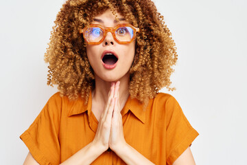 Surprise expression, young woman with curly hair in orange blouse, hands clasped, excited look...