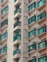 In this bustling area of Hong Kong, numerous residential apartments display distinct balcony styles, with many units featuring colorful curtains and air conditioning units, typical of urban living.