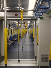 The interior of a train carriage is captured with empty blue seats and yellow handrails,...